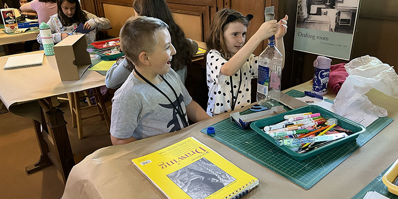 Two campers excitedly attempt to create a miniature version of the Home and Studio’s playroom inside a water bottle.